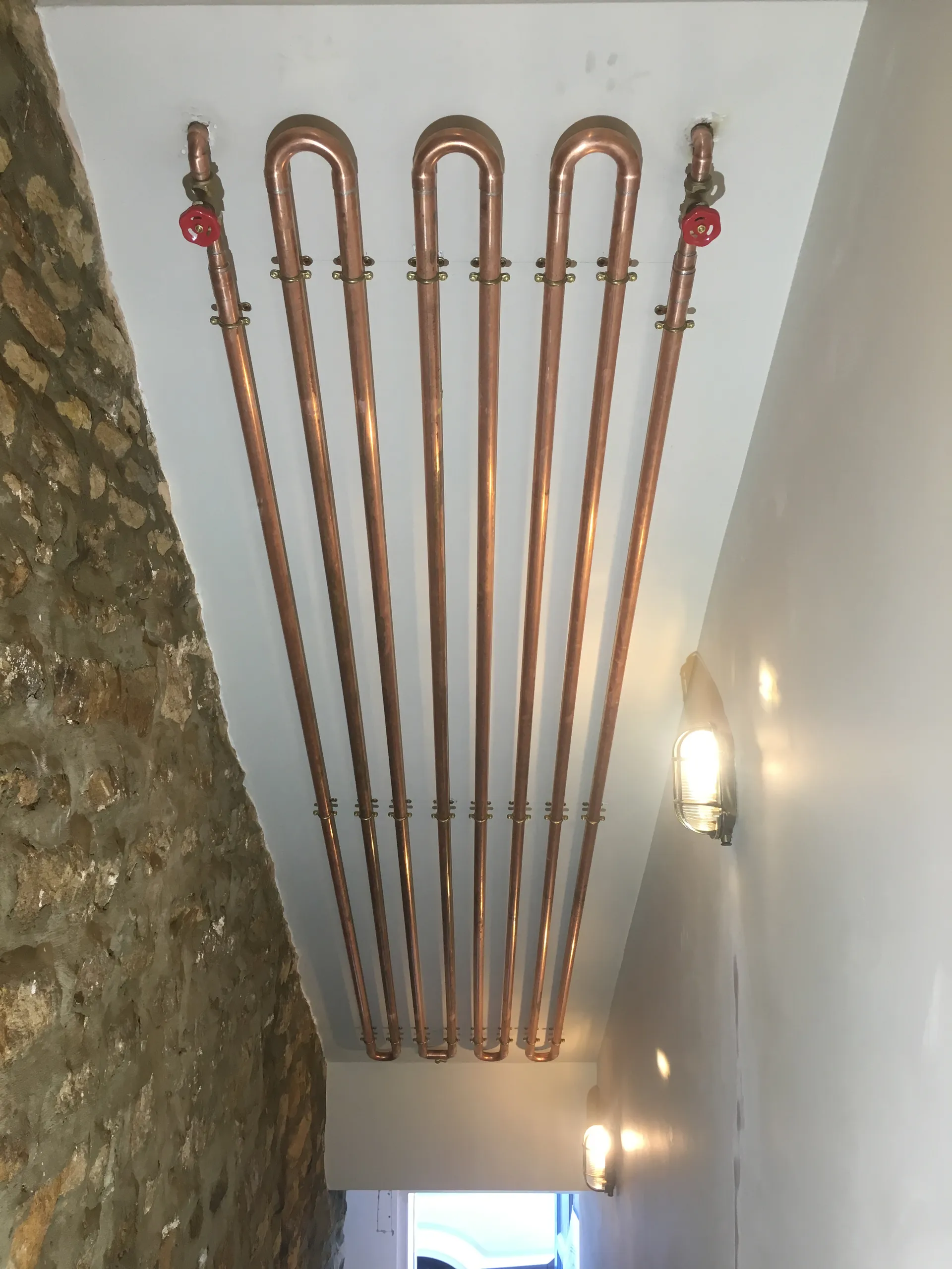 Striking polished copper serpentine pipe feature spanning a white wall above a stone floor.