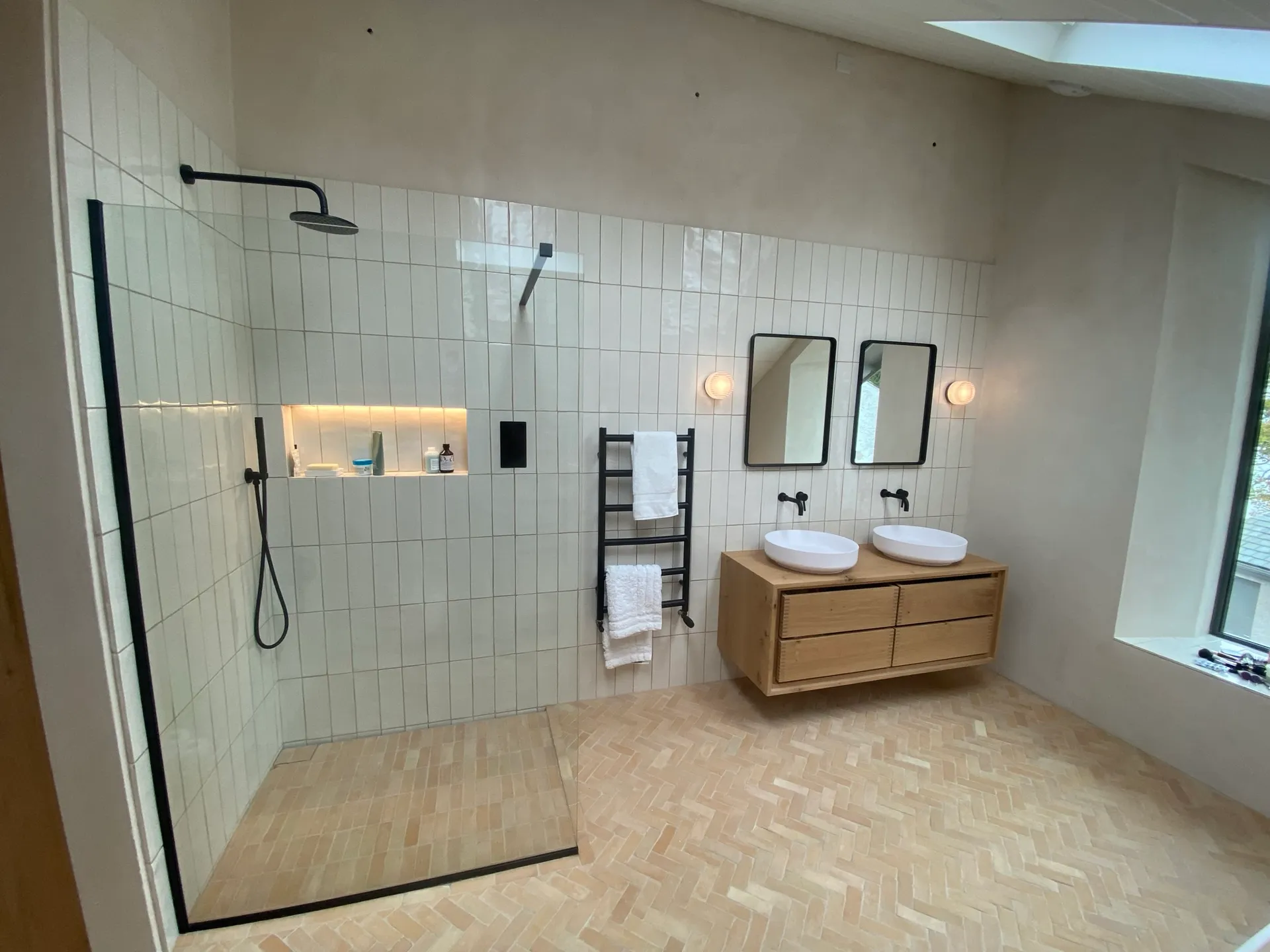 Premium ensuite with a black-framed walk-in shower, lit niche, twin white vessel basins on an oak vanity and two black-framed mirrors.