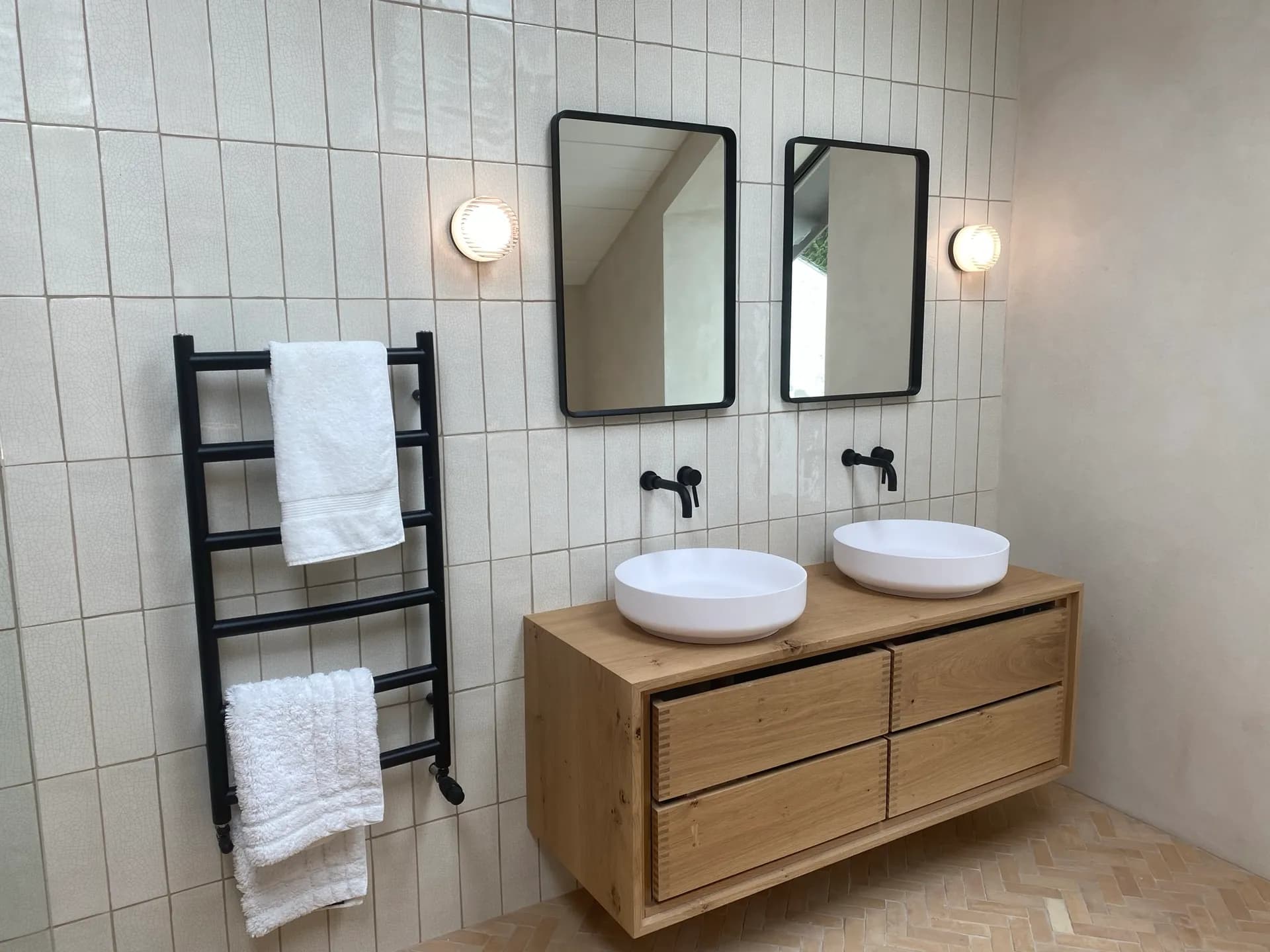 Twin white vessel basins on an oak floating vanity with wall-mounted black taps and black-framed mirrors.