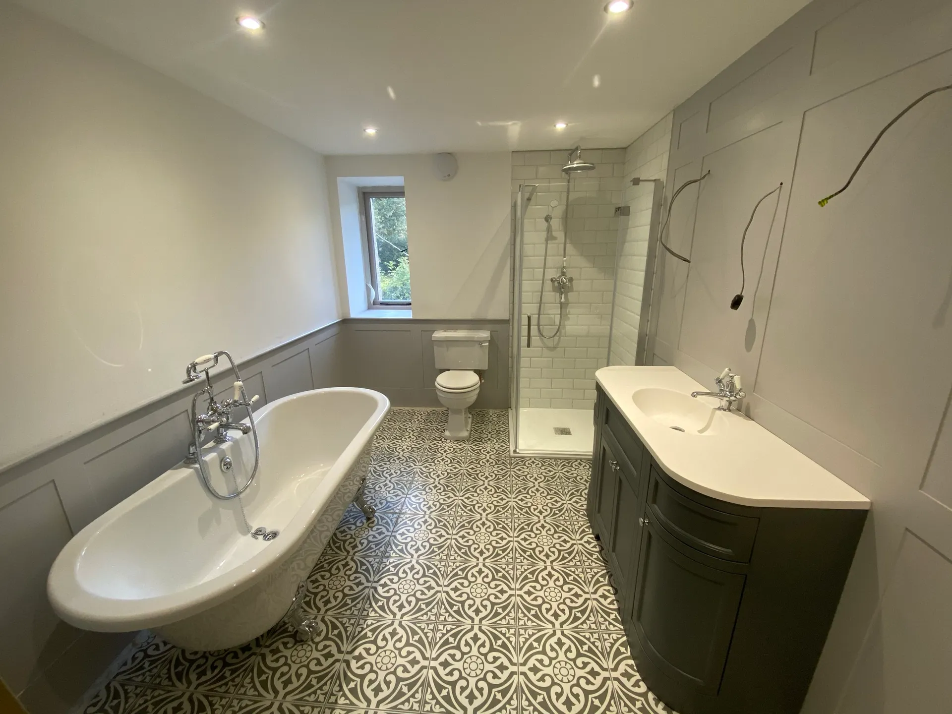 Wide view of a bright bathroom with a roll-top clawfoot bath, a glass corner shower enclosure and a close-coupled toilet.