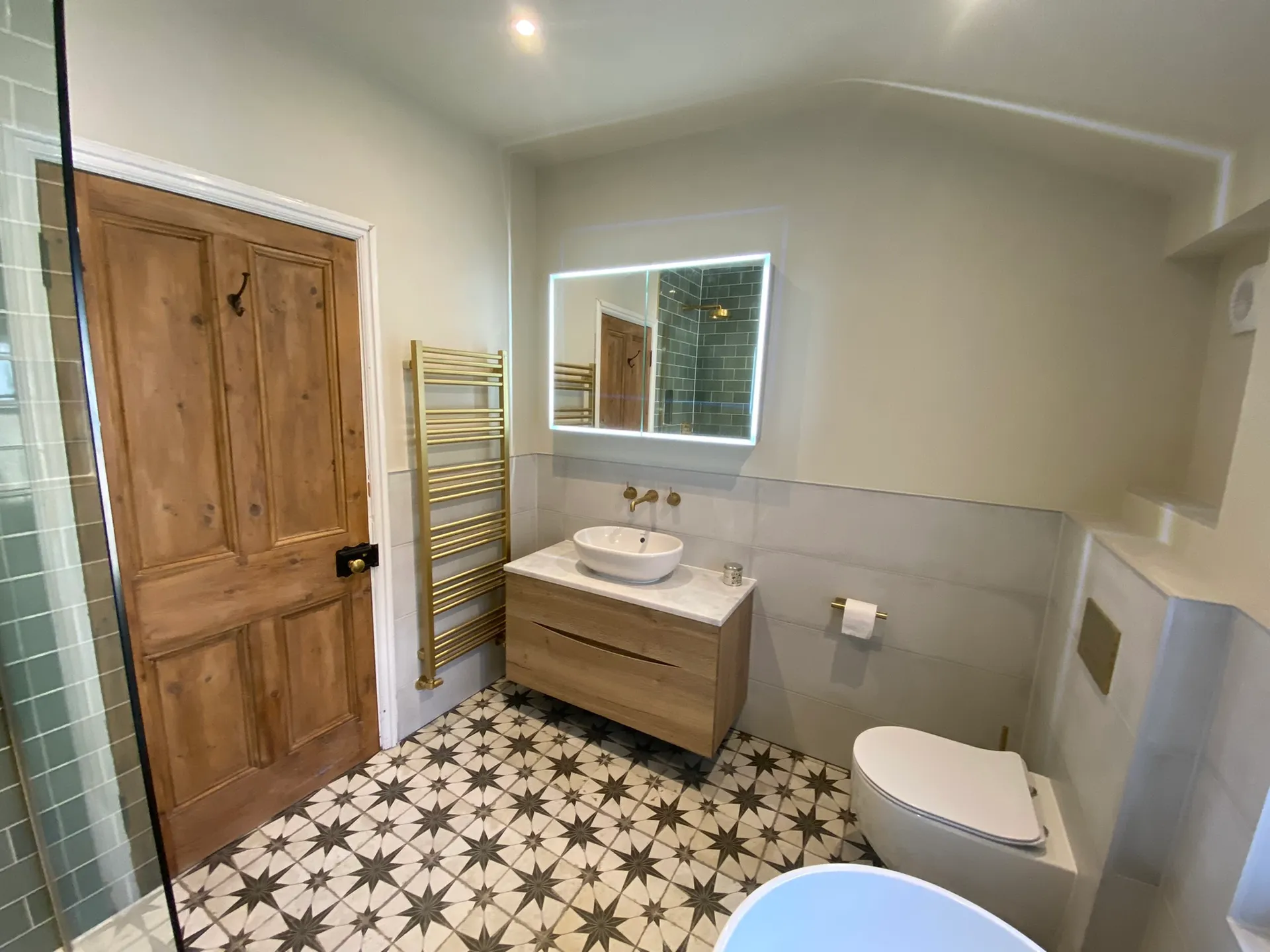 Wood-effect wall-hung vanity with a white countertop basin, backlit LED mirror and a tall brushed-brass ladder radiator.