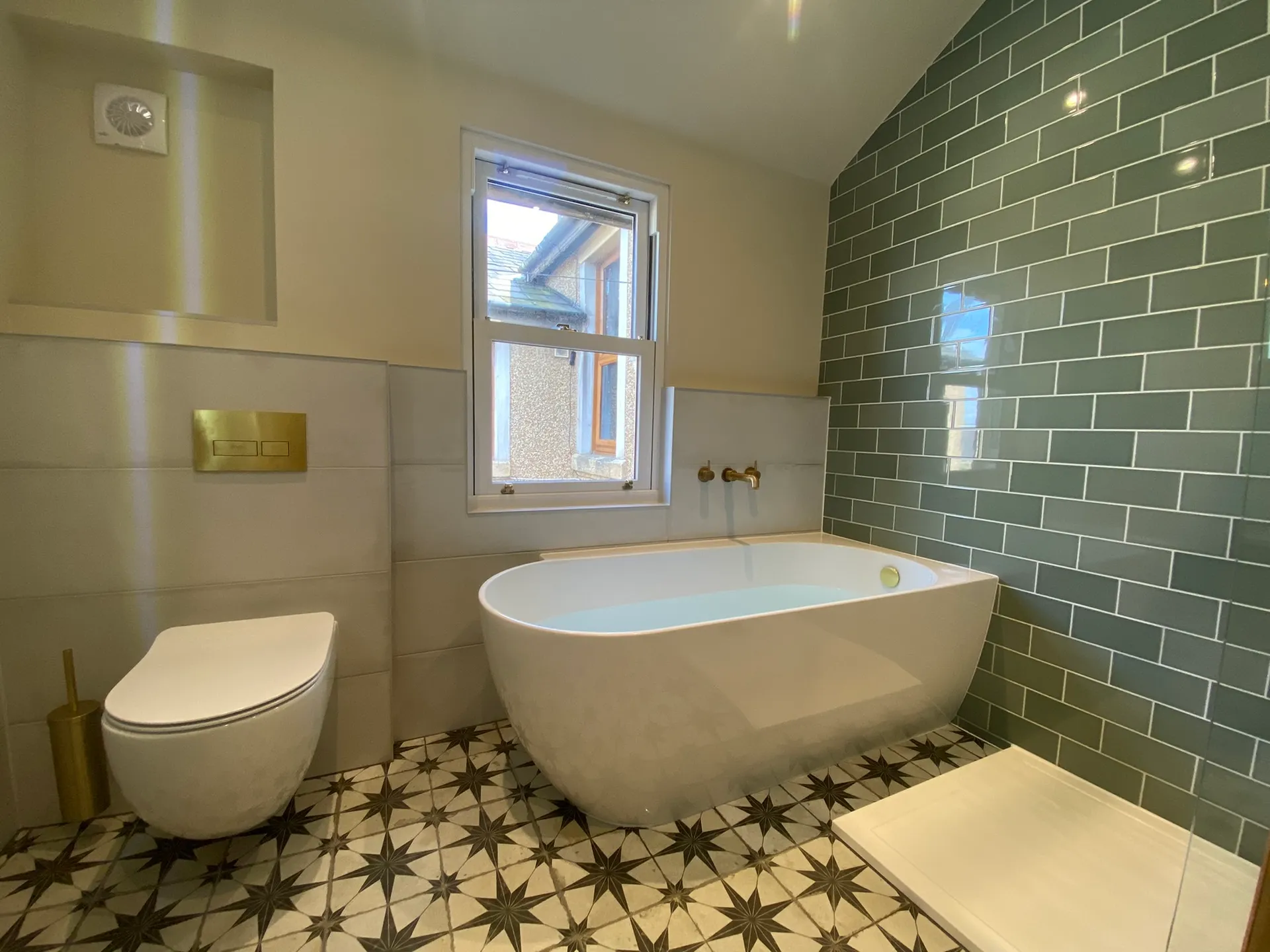 Finished bathroom with a white freestanding bath under a sash window, sage-green metro-tiled feature wall and star-pattern floor tiles.