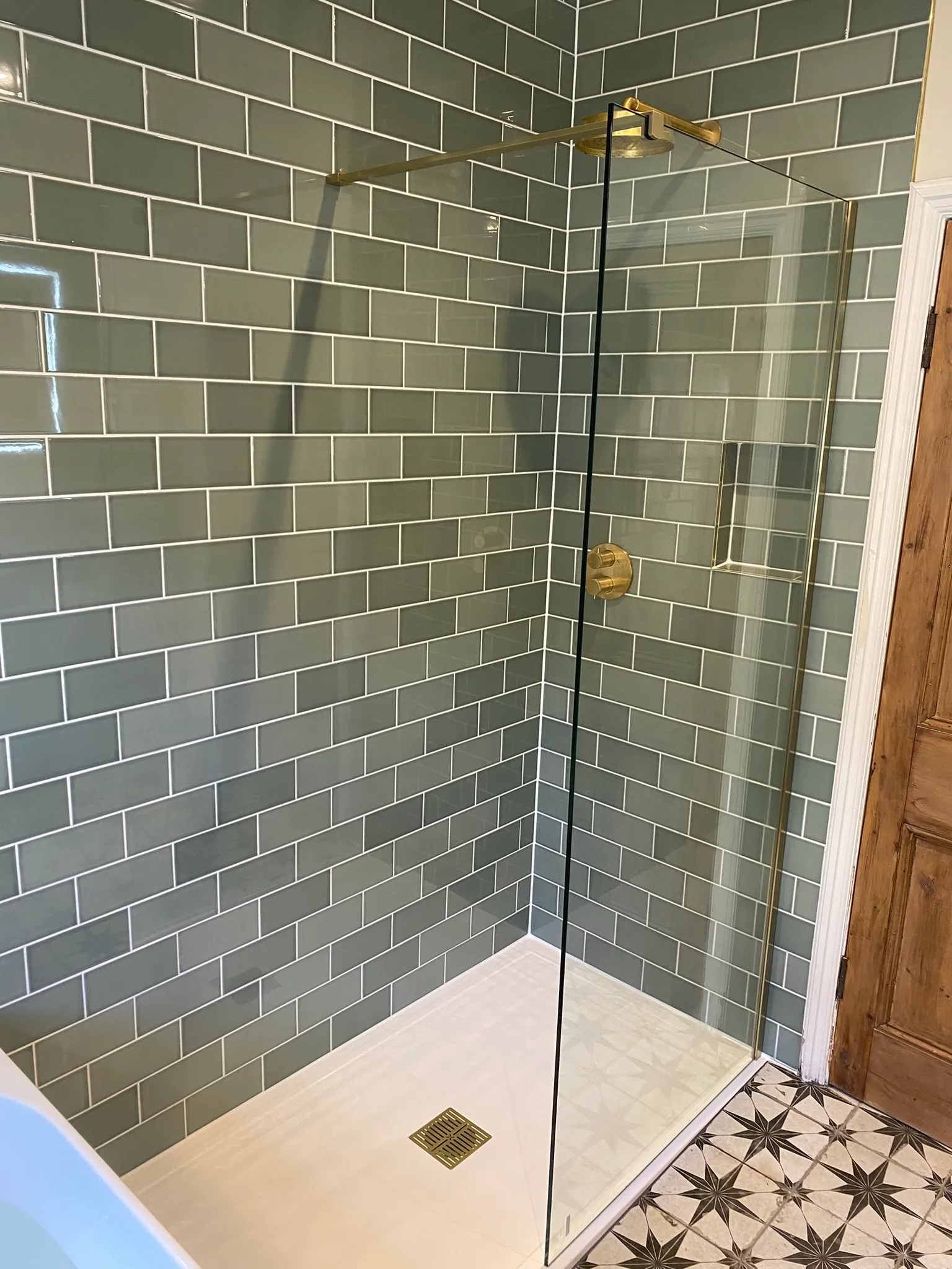 Sage-green metro-tiled walk-in shower with a brushed-brass rainfall head and thermostatic mixer valve.