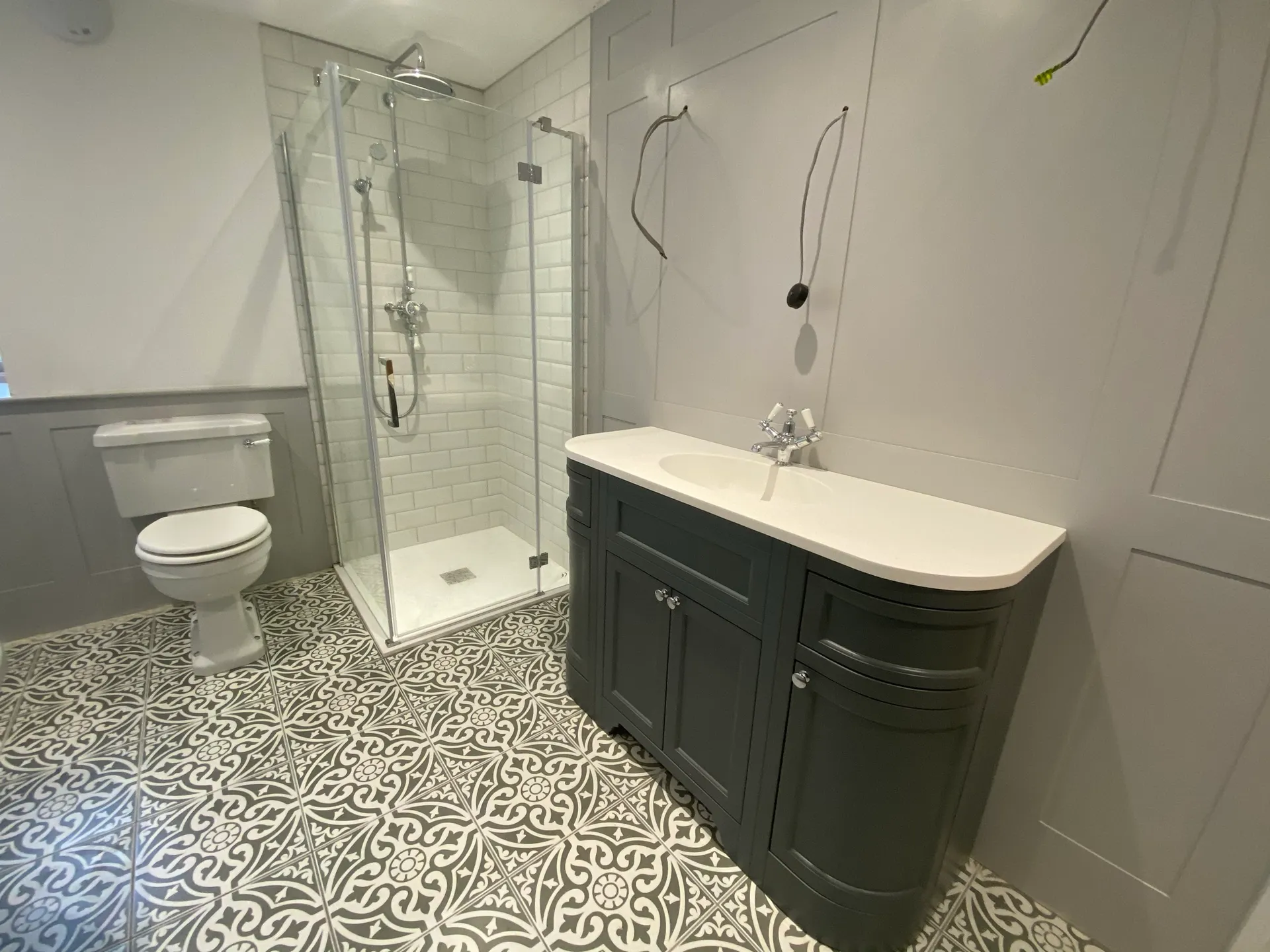 Grey shaker-style vanity with a white inset basin beside a glass corner shower with white subway tiles and a chrome rainfall head.