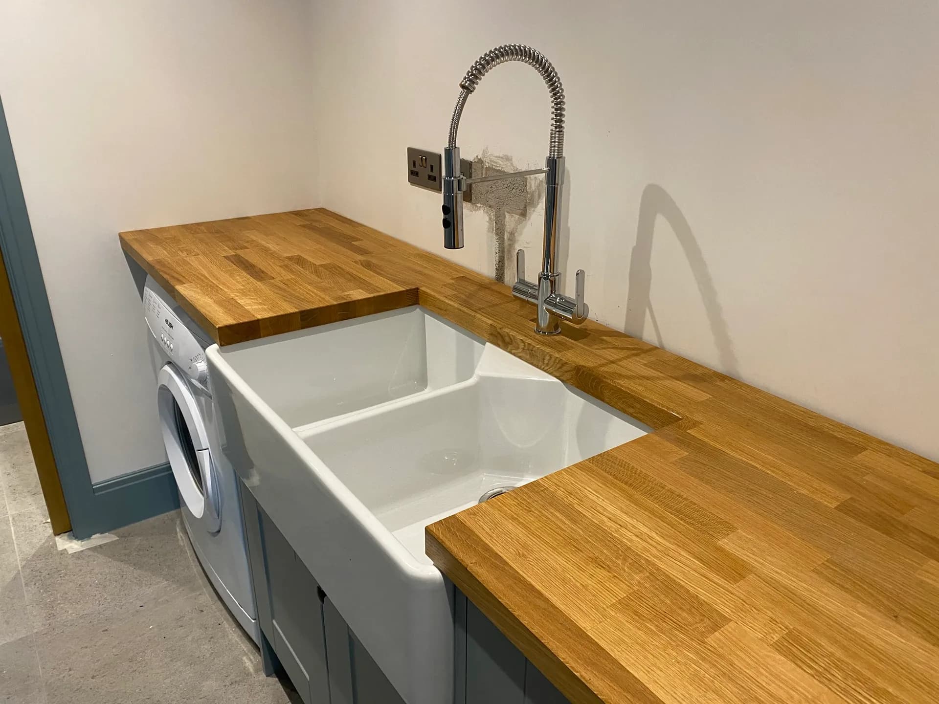Finished utility area with an oak butcher-block worktop, a white ceramic double butler sink and a chrome tap.